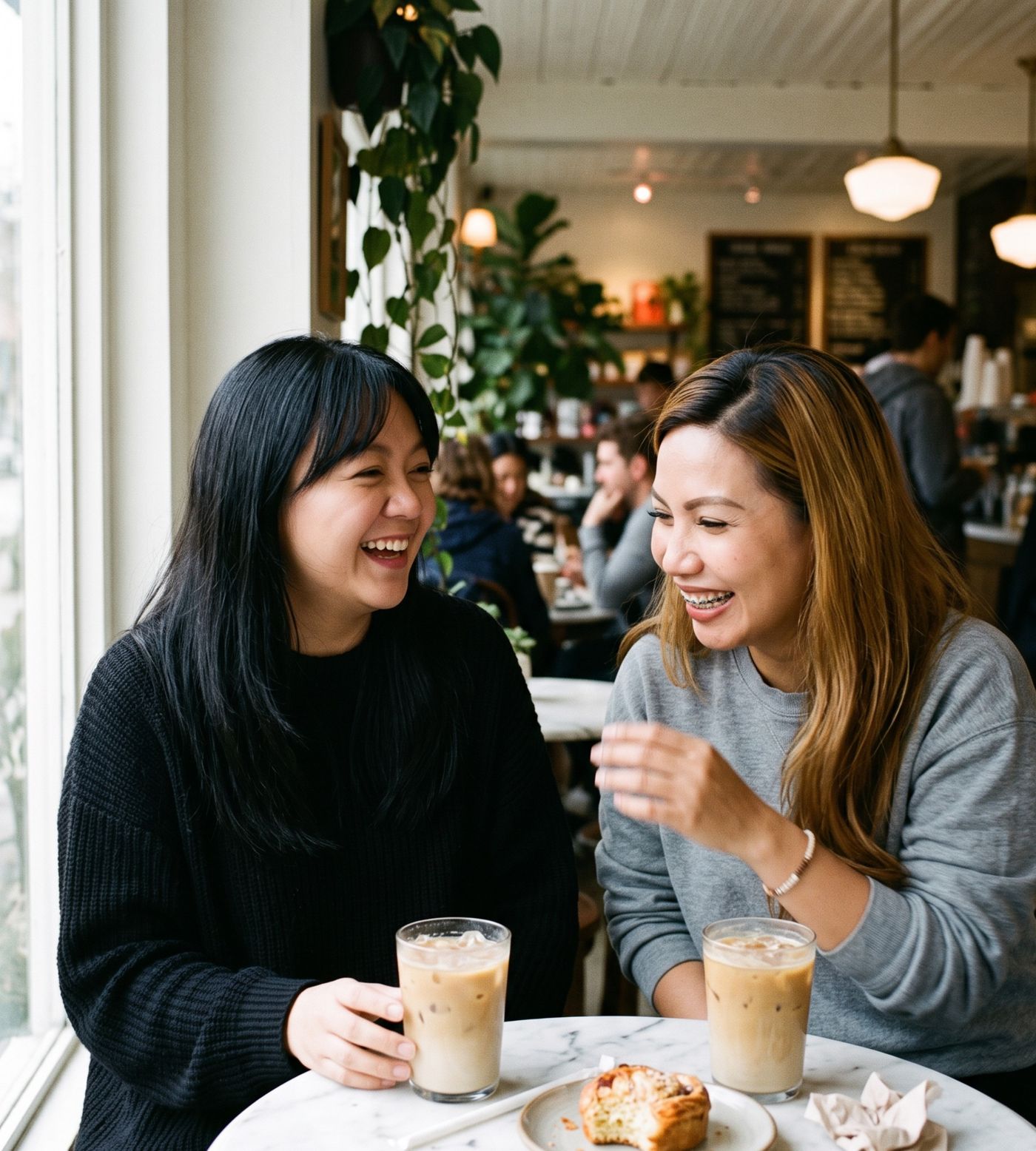 Dimple and Machu laughing over iced lattes at a café table