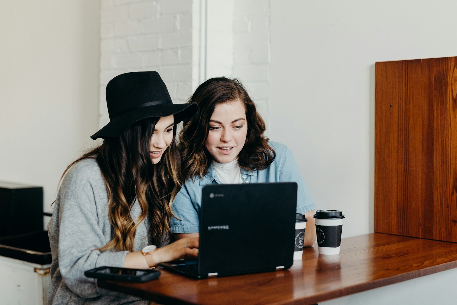 Two women working side by side at one laptop