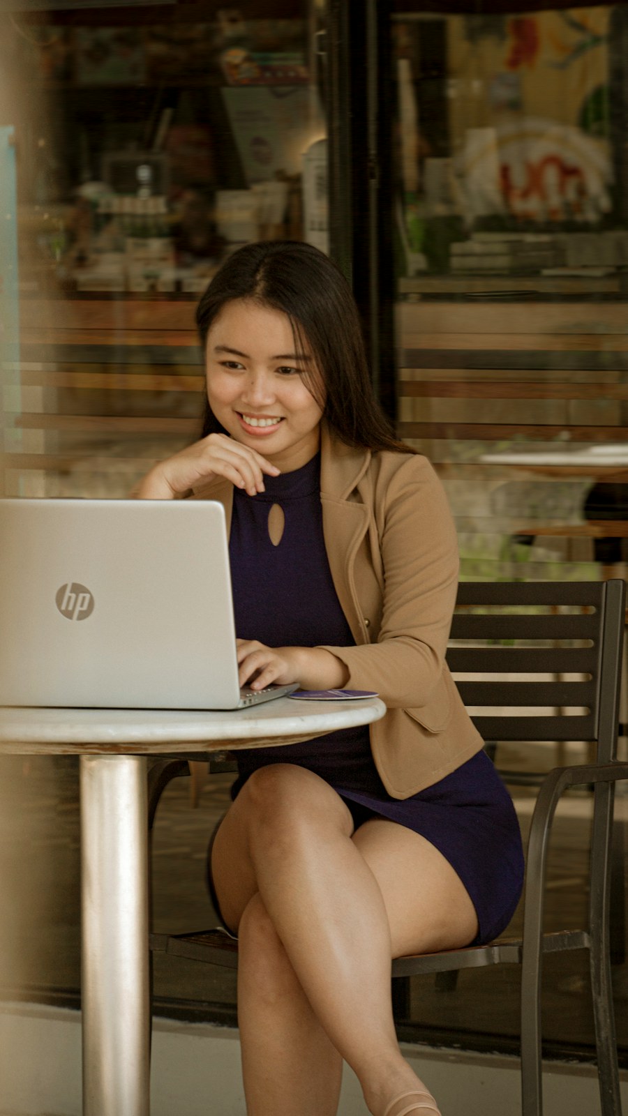 A woman in a blazer working on her laptop at a café table